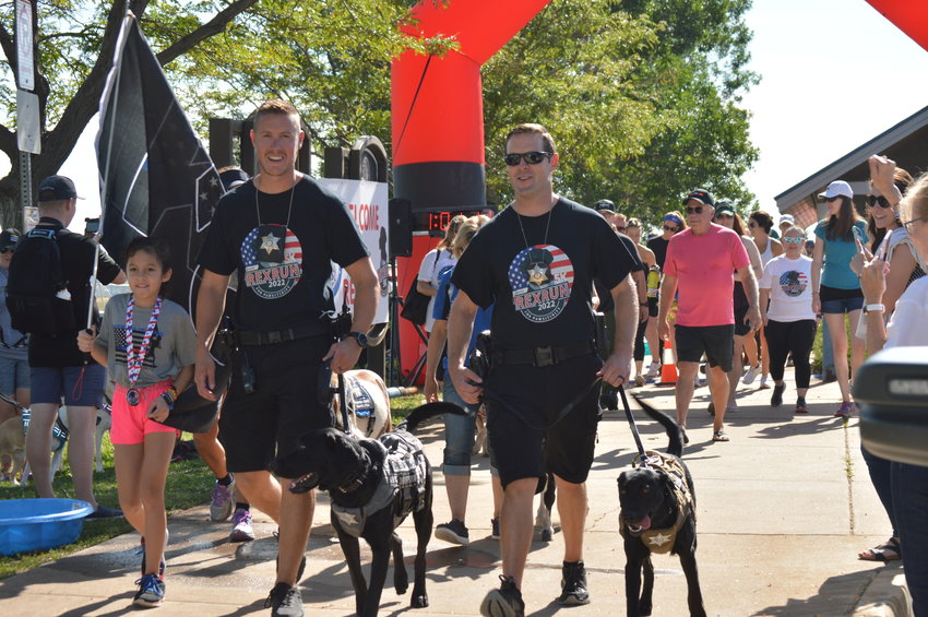 The “RexRun for PAWSitivity” event, held Aug. 6, 2022, at Dove Valley Regional Park, featured a 5K walk. Leading the group are School Resource Officer Deputy Travis Jones with therapy dog Zeke, right, and School Resource Officer Deputy John Gray with therapy dog Rex, left.